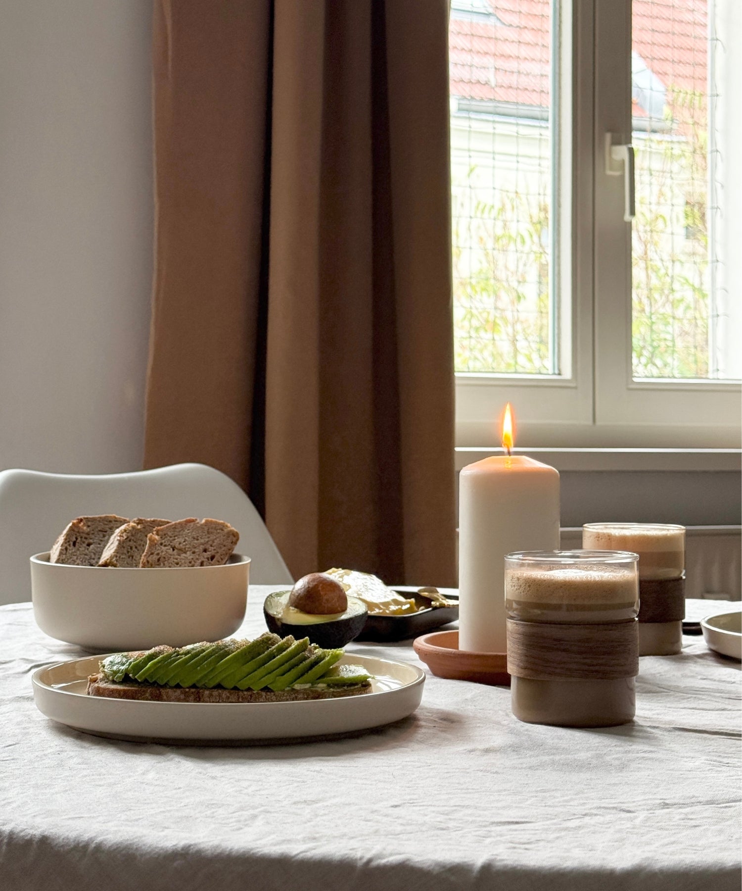 Herbstliche Tischdeko mit Brot, grünen Bohnen, Avocado, brennender Kerze und Gläsern in Naturfarben