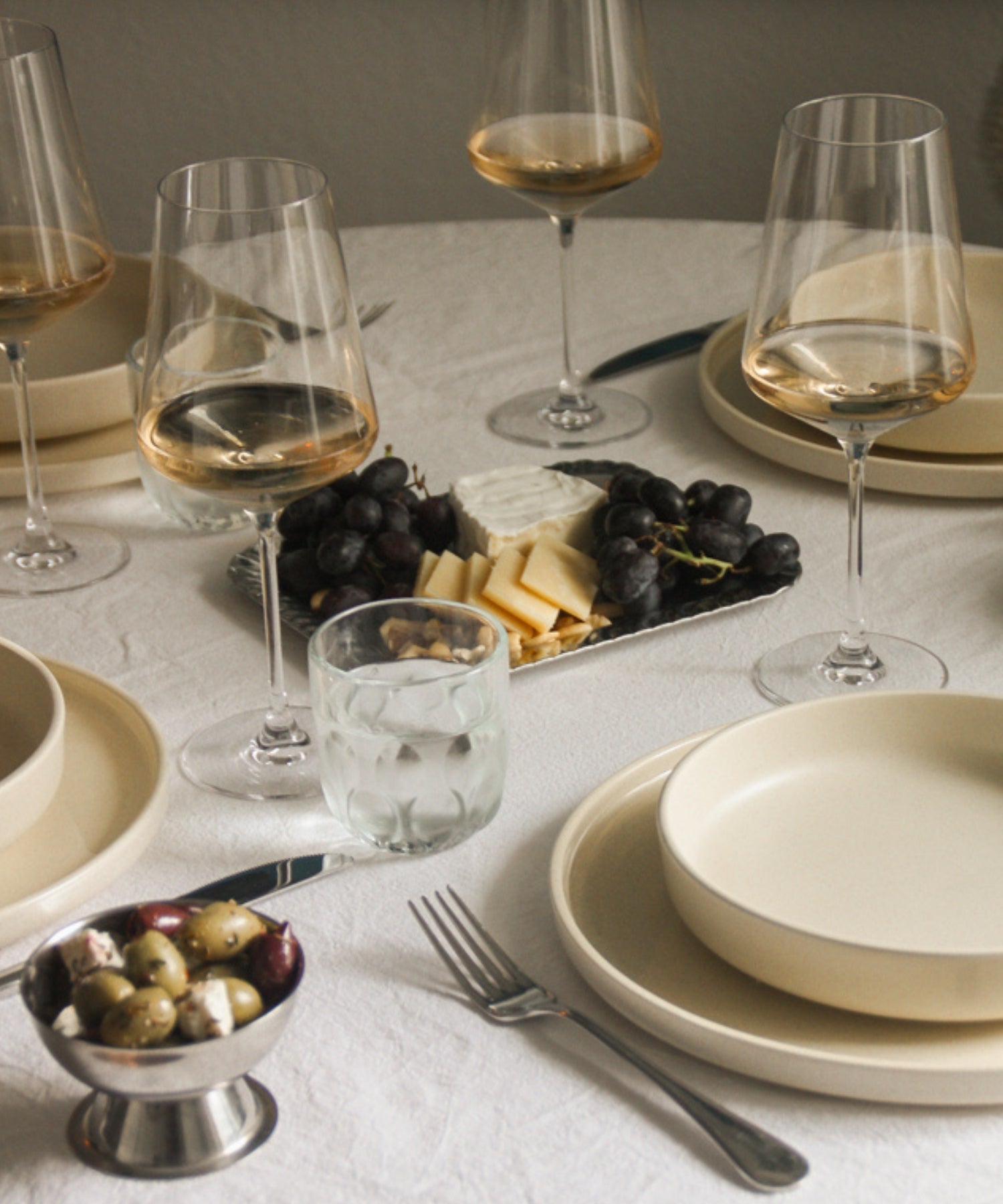 Elegant gedeckter Tisch mit Weingläsern, Tellern, Besteck, Trauben, Käse und Oliven in warmen Herbsttönen