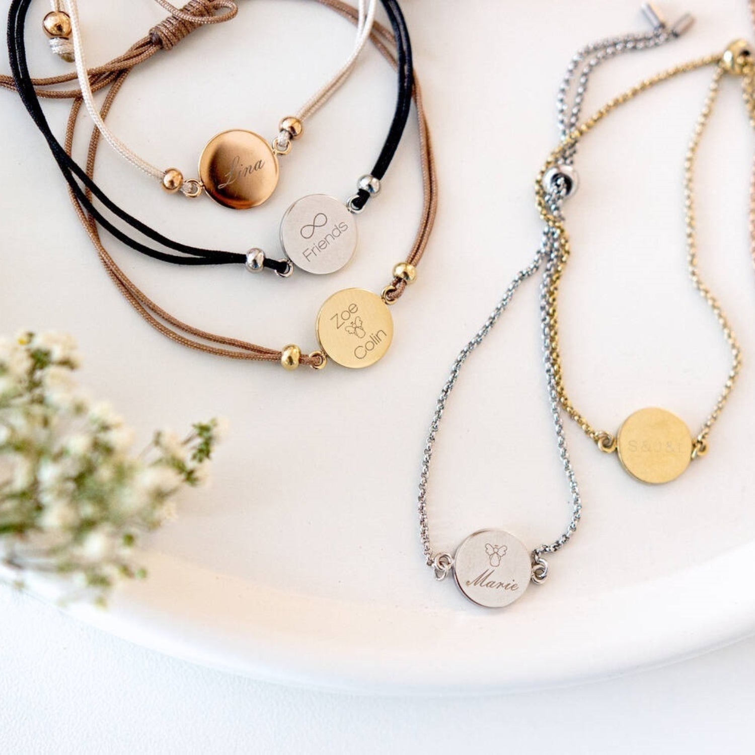 Mehrere gravierte Armbänder in Silber, Gold und mit Lederband auf weißem Untergrund
