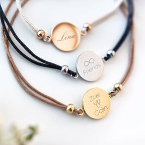 Drei Armbänder mit gravierten Plaketten in Gold, Silber und Rosegold auf weißem Hintergrund