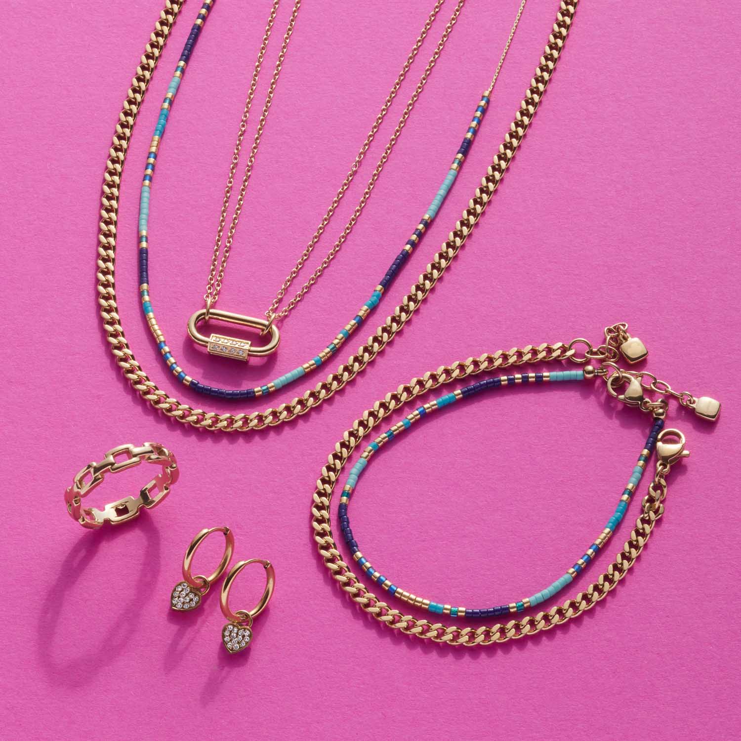 Goldener Schmuck mit Ketten, Armband, Ring und Ohrringe auf rosa Hintergrund