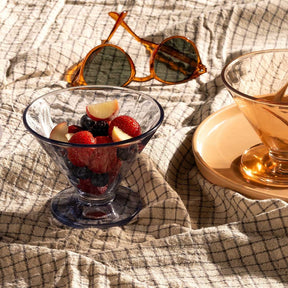 Eisschale mit roten Früchten auf Tischdecke, Sonnenbrille und Getränk sichtbar