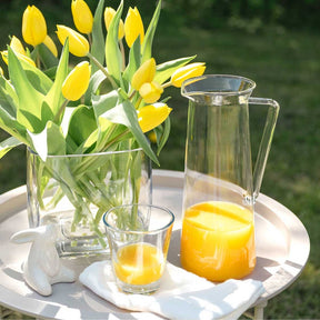Gelbe Tulpen in Vase auf Tisch mit Orangensaft und Glas im Freien