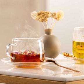 Teetasse TÈ PER TE mit rotem Tee auf weißem Tablett, Blumenvase und Teeglas im Hintergrund