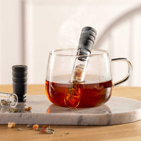 Teetasse TÈ PER TE mit Tee gefüllt auf Marmortablett, daneben Teefilter und Teedose