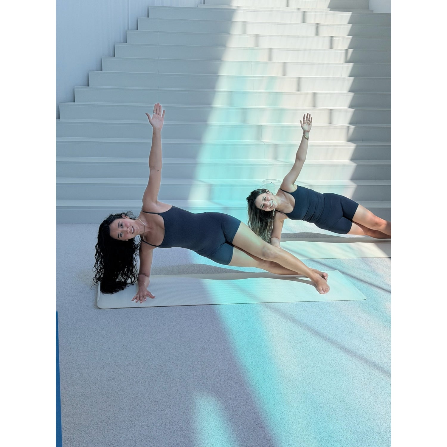 Zwei Frauen praktizieren Pilates auf hellem Untergrund vor Treppenstufen