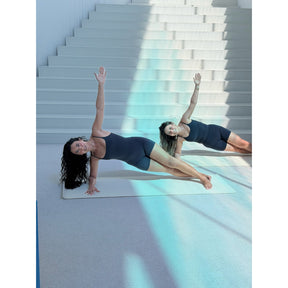 Zwei Frauen praktizieren Pilates auf hellem Untergrund vor Treppenstufen