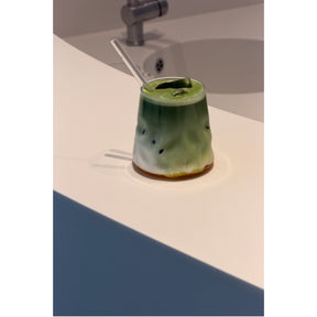 Grünes Matcha-Getränk im Glas auf Badezimmer-Waschtisch mit Strohhalm