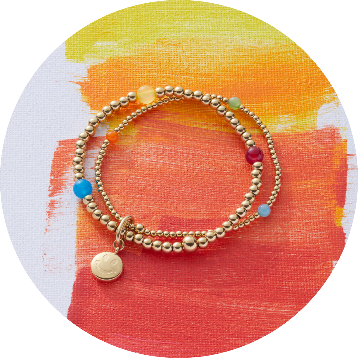 Zweireihiges Armband mit kleinen Kugeln und farbigen Schmucksteinen liegt auf einer farbenfrohen Leinwand mit Gelb-, Orange- und Rottönen.