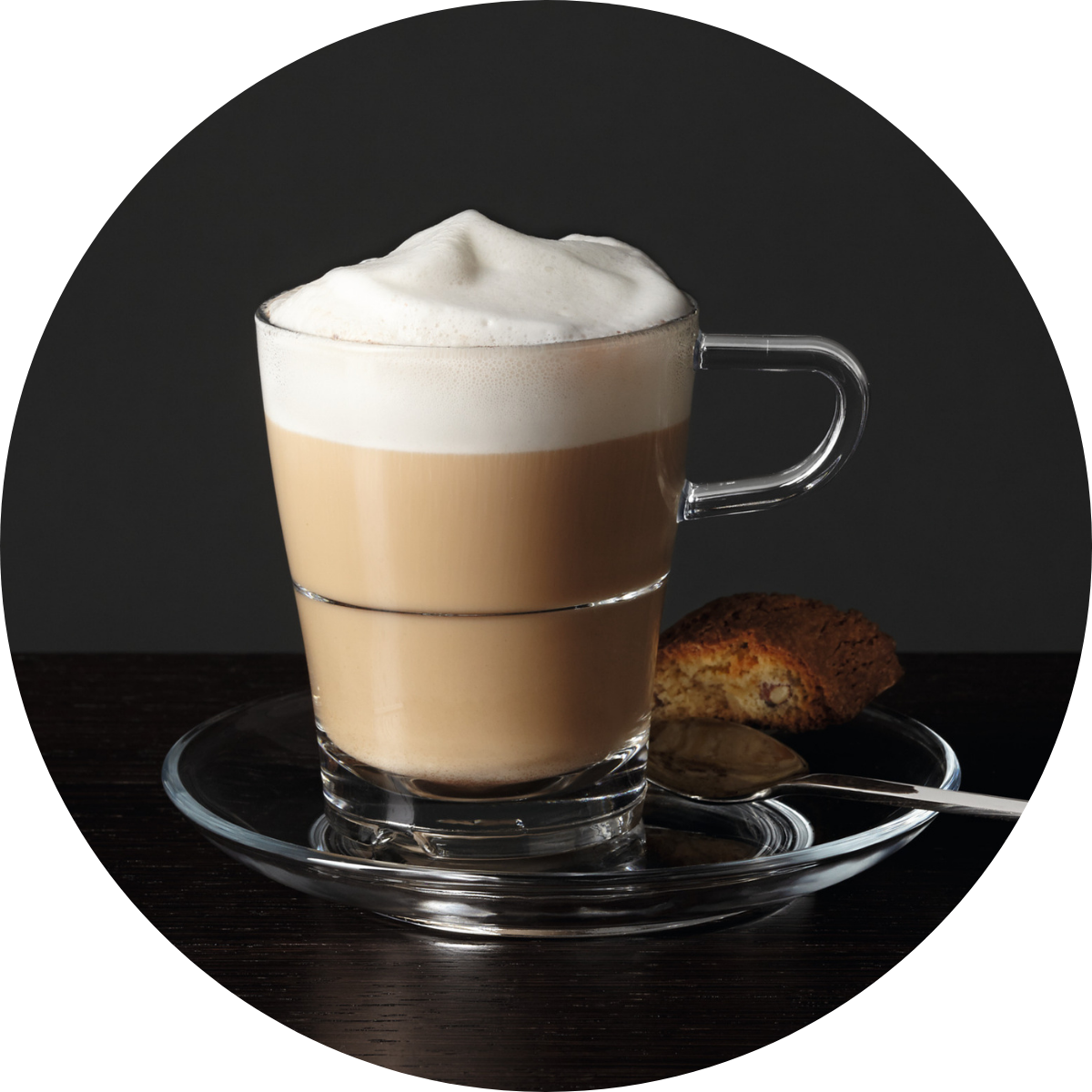 Cappuccinoglas mit dickem Milchschaum auf Untertasse mit Gebäck.