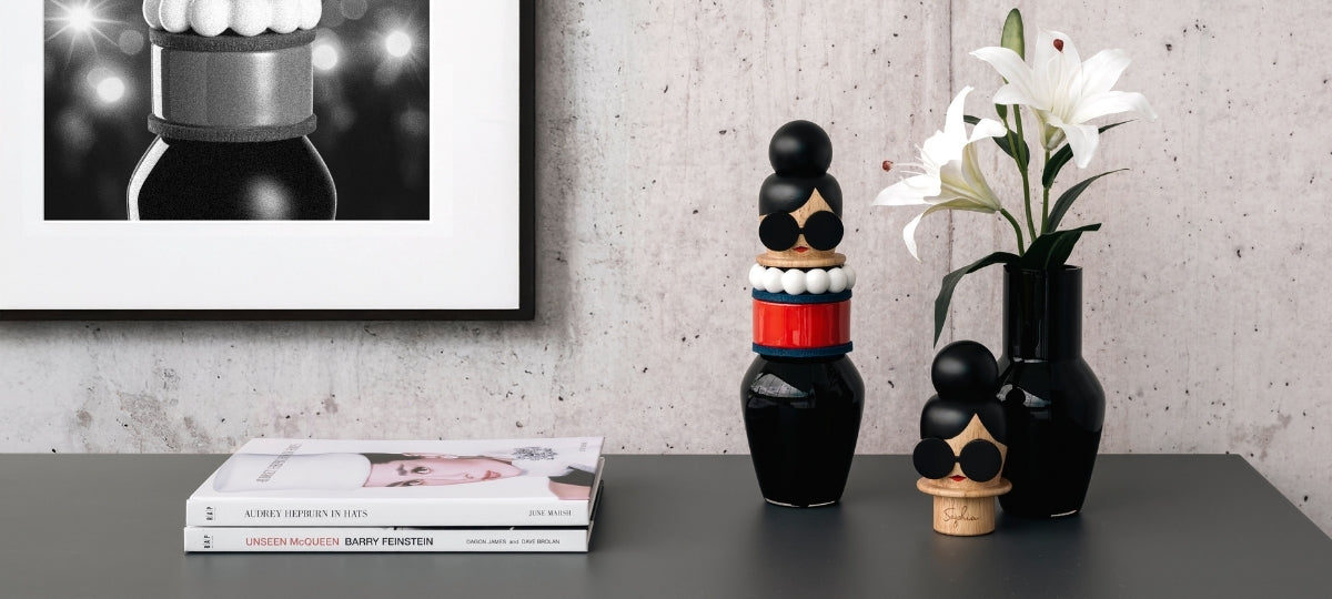 Schwarze Dekofiguren und Vasen mit weißen Blüten auf grauem Tisch, Bücher und Wandbild im Hintergrund
