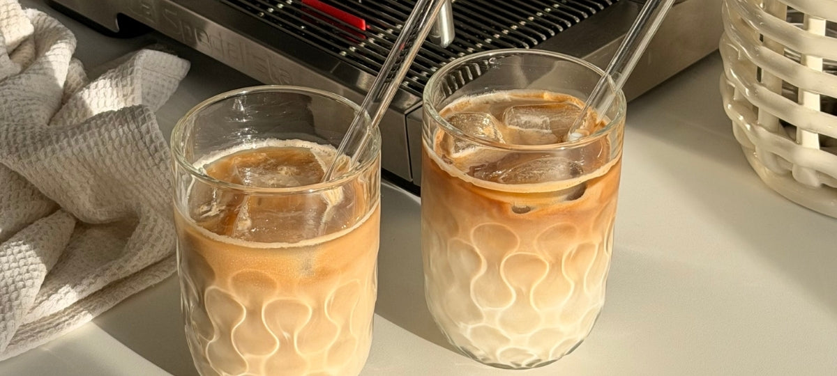 Zwei Gläser mit geometrischem Muster gefüllt mit Getränk und Eiswürfeln auf heller Oberfläche