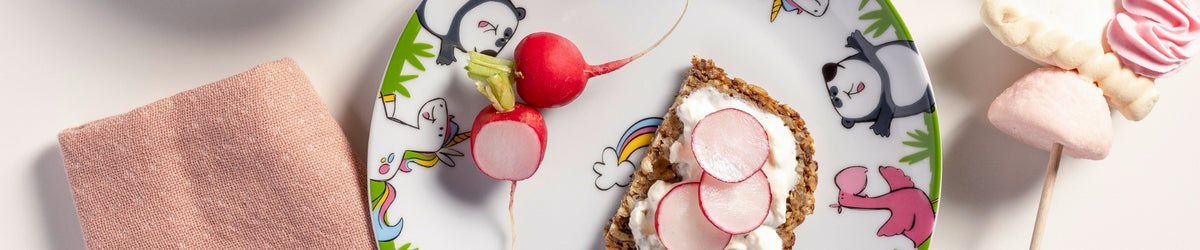 Kindergeschirr mit buntem Muster, Radieschen auf Toast, rosa Handtuch, Marshmallows und Lollipops auf weißem Hintergrund