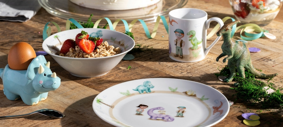 Kindertablett mit bunten Motiven, Müslischale mit Früchten, Dinosaurier und Spielfiguren auf Holztisch