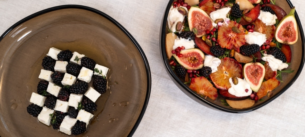 Zwei Servierteller mit eleganter Anrichtung: schwarze und weiße Käsewürfel im Schachbrettmuster, bunte Früchte mit Feigen, Beeren und Creme