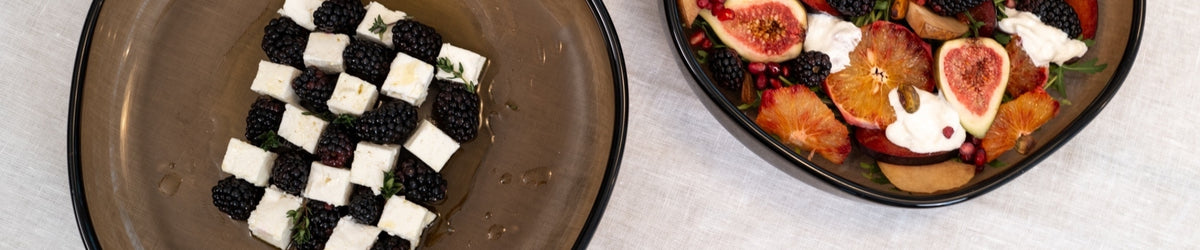 Zwei Glasteller mit Servierschüsseln: Einer mit Mozzarella und schwarzen Beeren im Schachbrettmuster, einer mit Feigen, Früchten und Mozzarella
