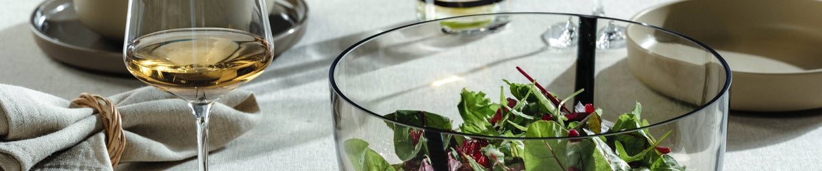 Elegantes Serviergeschirr mit Weinglas, Salatschüssel und Besteck auf hellem Tischtuch in naturaler Atmosphäre